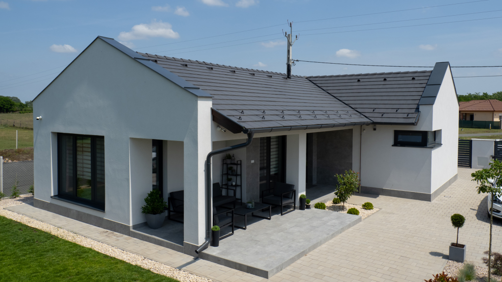 Zenit Gránit tetőcserép újépítésű házon fehér vakolattal szürke térkővel, kerti növényekkel, zöld gyeppel. Zenit Gránit tetőcserép újépítésű házon fehér vakolattal szürke térkővel.